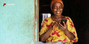 A smiling Woman using a non-internet phone to make financial transactions.